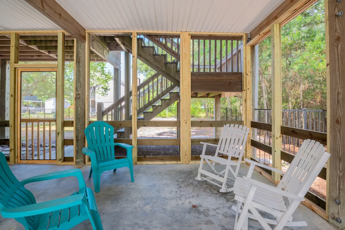 A spacious screened back porch featuring a mix of turquoise and white chairs arranged for group seating. The porch is enclosed by screened walls, allowing in gentle breezes and natural light. Views of surrounding greenery invite the outdoors in. The space feels casual and tranquil, ideal for sunset cocktails, meals, or unwinding with loved ones.