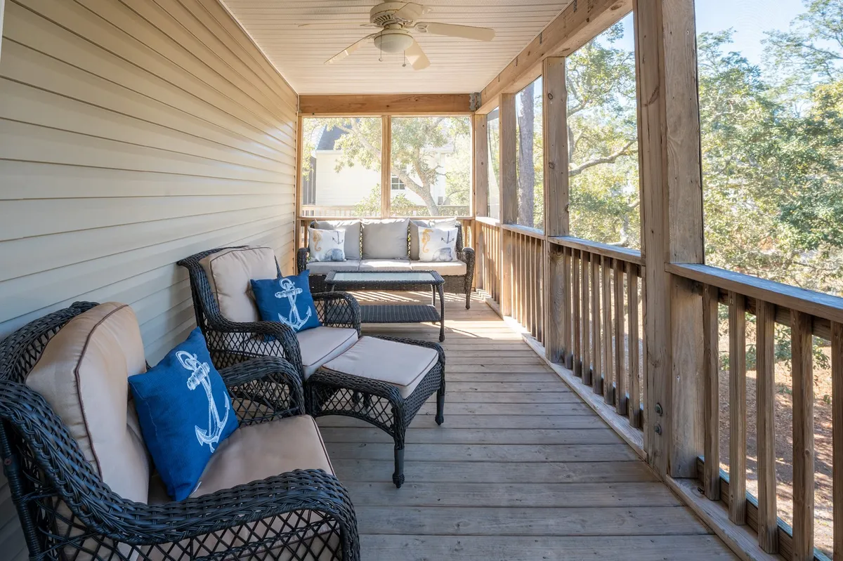 A cozy seating area on a porch featuring wicker chairs with decorative anchor-themed cushions, set beside a wooden railing. The scene invites you to relax while enjoying a refreshing breeze and views of the outdoors, suggesting a transitional space between the home and the yard.