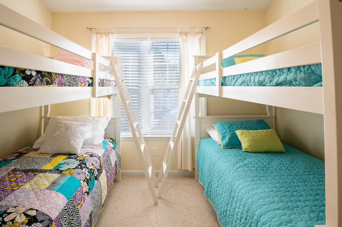 A cheerful kids’ bunk room filled with colorful quilts, bright natural light streaming through the window, and plenty of space for playful activities such as games or reading.