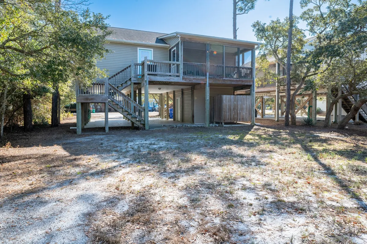This exterior shot focuses on a welcoming deck with stairs leading down to the yard, surrounded by lush trees. The deck is set up for outdoor relaxation and gatherings, with ample space for beach chairs, picnics, or lawn games, creating an inviting environment for family activities.