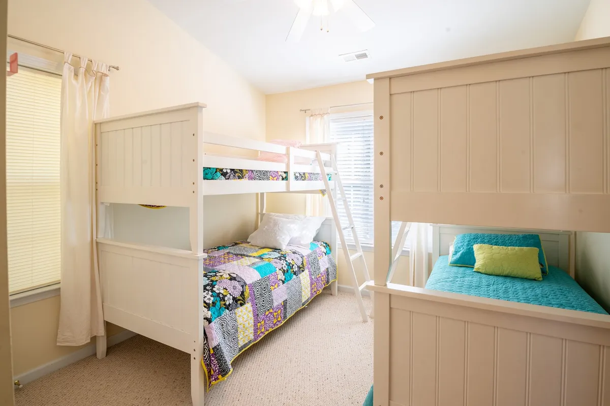 A vibrant bedroom with bunk beds covered in colorful quilts, bathed in natural light from a large window. The playful atmosphere encourages shared experiences, perfect for kids or families traveling together. The arrangement invites activities like reading, chatting, or playing together.