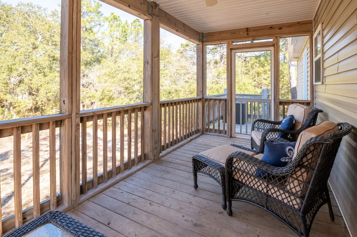 A tranquil screened-in porch with wicker chairs overlooking a wooden deck, providing an inviting spot for reading or observing nature. The porch hints at views of the surrounding yard and offers a peaceful space connected to the outdoors.