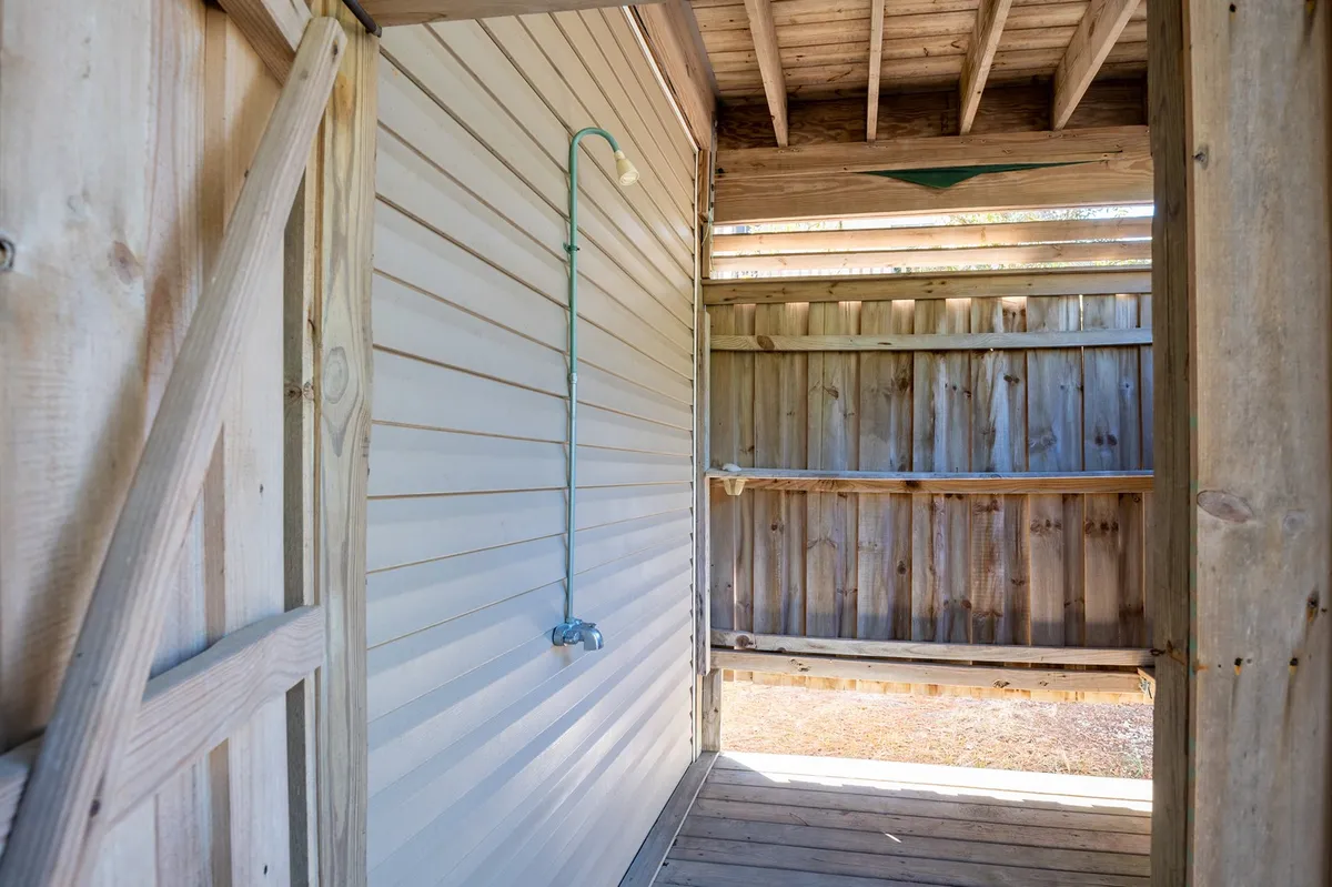 A spacious and open interior with exposed wooden beams and visible plumbing. The room feels airy and inviting, with plenty of natural light streaming in. There are comfortable seating options arranged for casual gatherings, and the open space encourages movement and interaction, suggesting a seamless flow to outside areas, such as a porch or backyard.