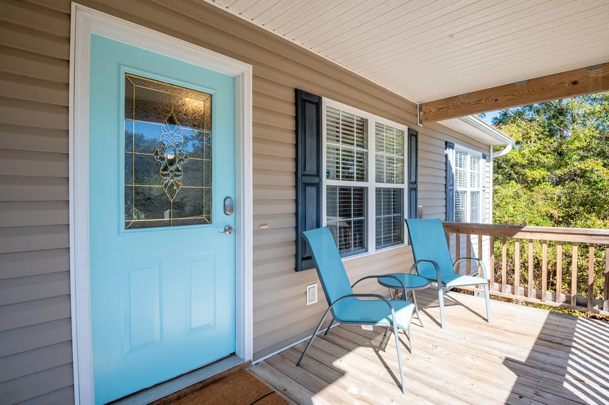 A welcoming exterior shot featuring a turquoise front door framed by blue chairs and a wooden railing. The porch is inviting—ideal for enjoying the fresh breeze and observing neighborhood activity after a day at the beach.