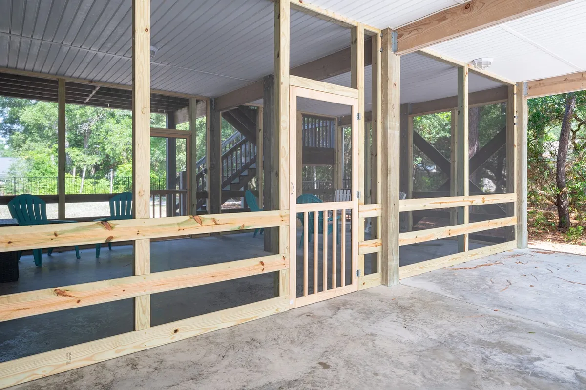 Another angle on a screened porch, this time featuring bright blue chairs and a wooden gate. The space is airy and inviting, with views of the surrounding greenery. The porch feels sociable and connected to nature, suitable for both quiet morning moments and lively evening gatherings.